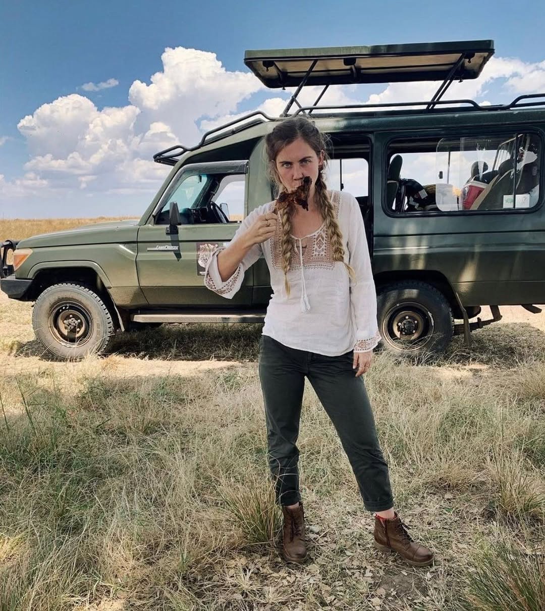 Guest standing near safari vehicle with pop-up roof in grassland having bush served lunch in the massai mara